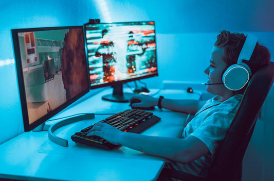 Person sitting at a desk with dual monitors and headphones, engaged in computer work or gaming.